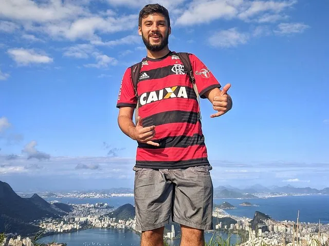 Smiling man in sports jersey standing with city and mountain background.