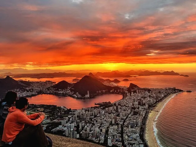 Two people sitting on a rock admiring a vibrant sunset over Rio.