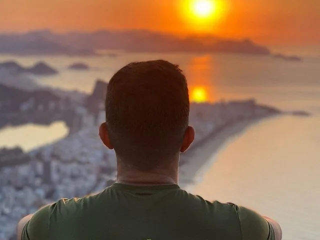 Back of a person's head looking at the sunset over the coast.