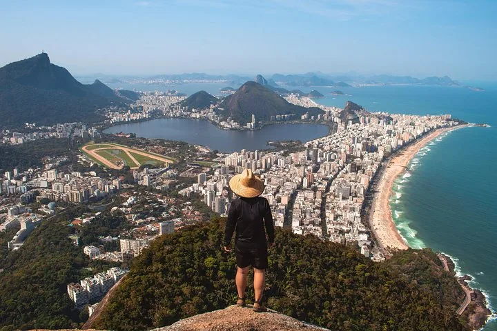 Persona con sombrero en una cima rocosa contemplando el paisaje y la costa de Río de Janeiro.