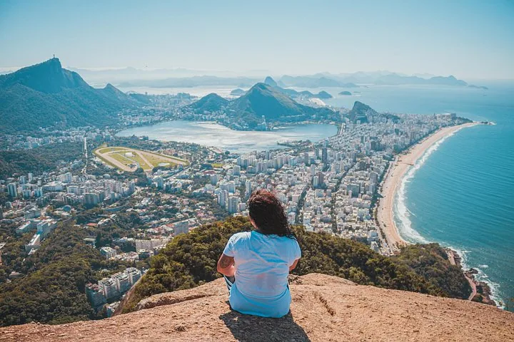 Personne assise au bord d'un rocher surplombant Rio de Janeiro et l'océan.
