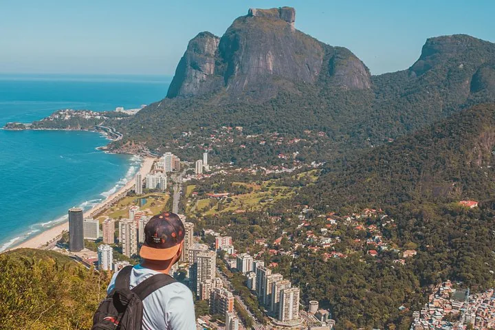 Personne avec un sac à dos contemplant le Morro Dois Irmãos et la vue sur la ville côtière.